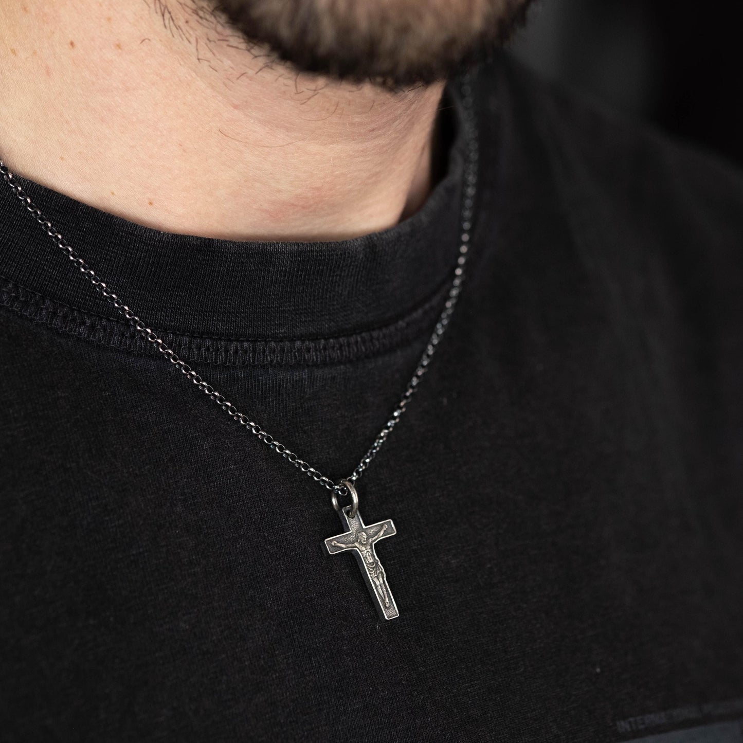 A silver cross pendant is worn on a black t-shirt.