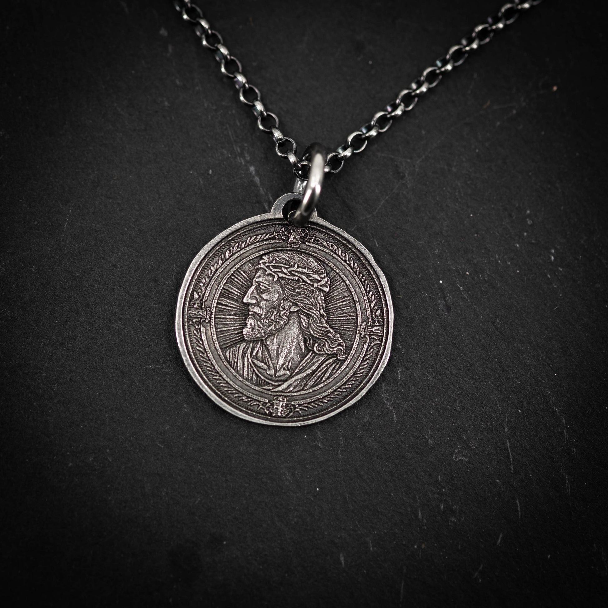 A silver-colored pendant featuring an engraved image of a man's profile, possibly a religious figure.