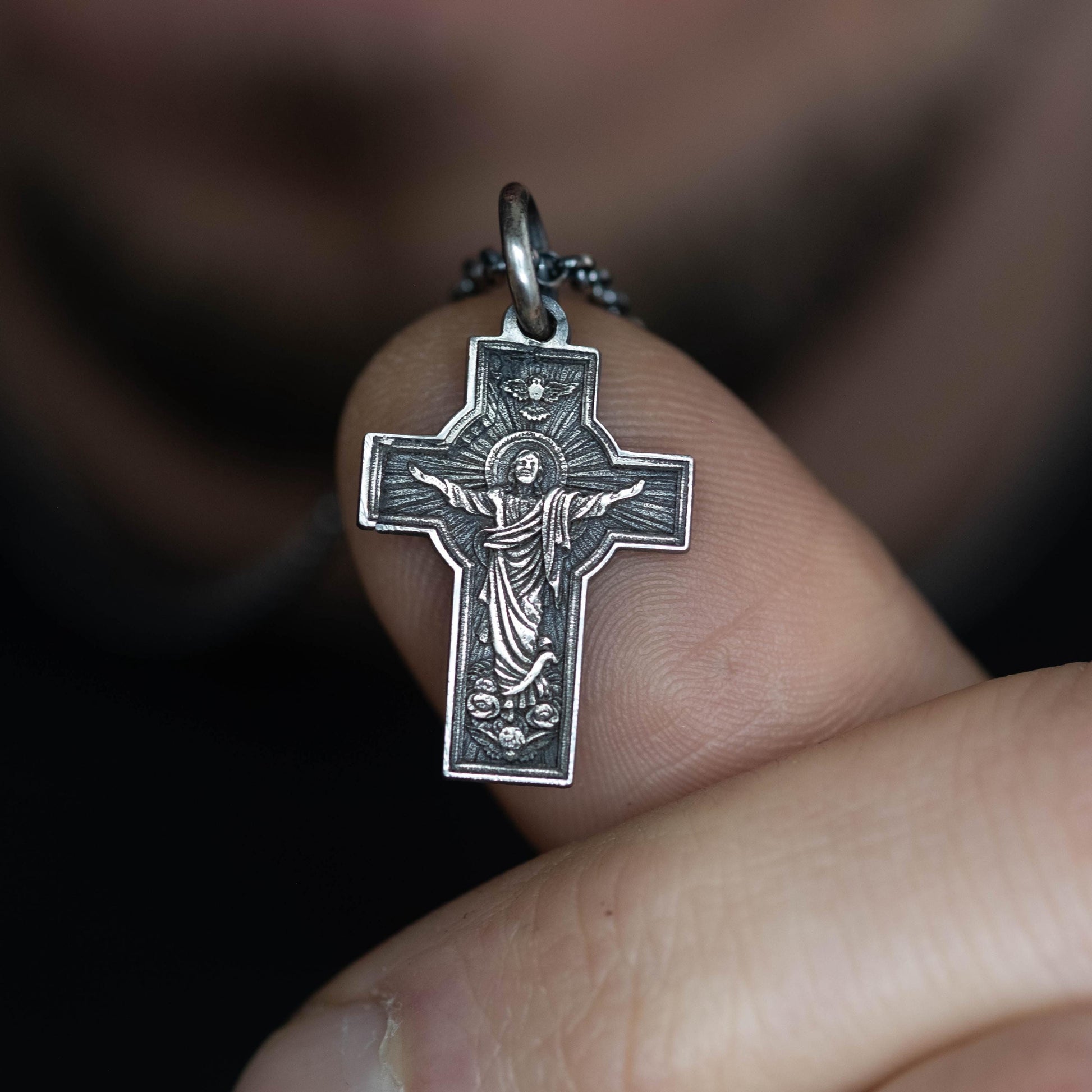 A person is holding a small silver cross pendant on their finger.