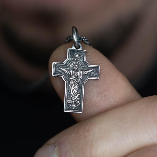A person is holding a small silver cross pendant on their finger.